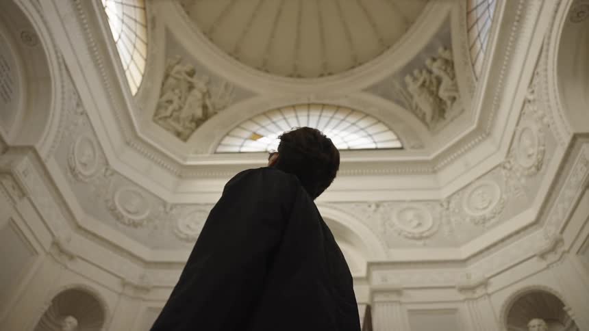 A man in a black coat looks up at the ornate ceiling of a museum rotunda
