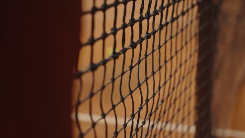 A tennis ball hits a clay court in dramatic slow motion as the camera racks focus from the net