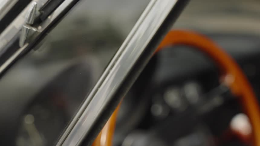 Slow rack focus from the vintage wooden steering wheel to the chrome windshield trim inside a classic car