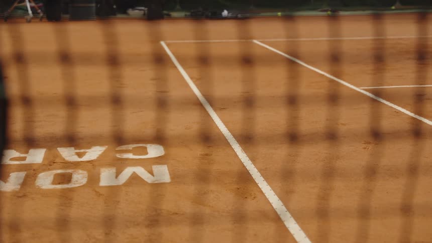 A close-up view of a tennis net slowly racks focus to reveal the empty professional clay court in the background