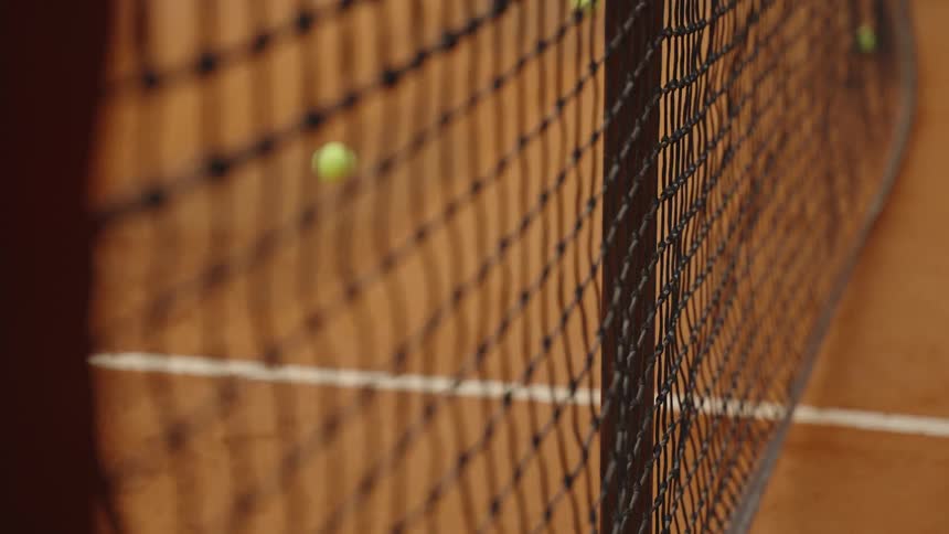 A tennis ball bounces in slow motion on a clay court as the focus pulls from the net to the ball