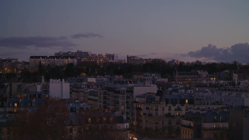 A serene wide shot of a European city skyline at dusk as apartment lights begin to twinkle on