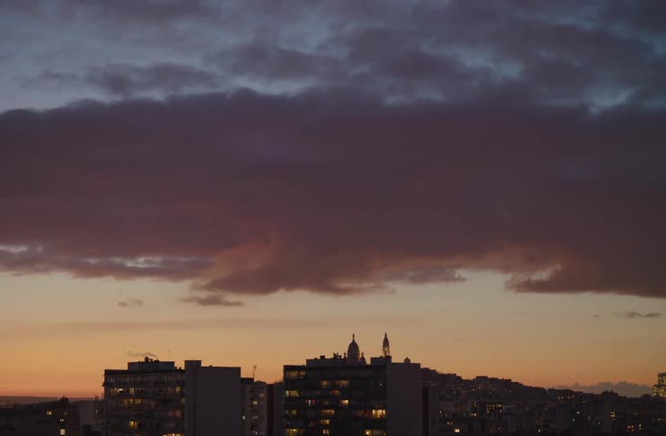 A static shot of a city skyline with apartment buildings silhouetted against a beautiful purple and orange sunset