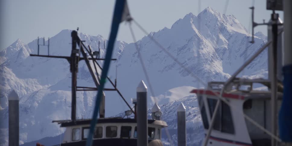 A scenic view of majestic snow-covered mountains towering behind boats docked in a tranquil harbor