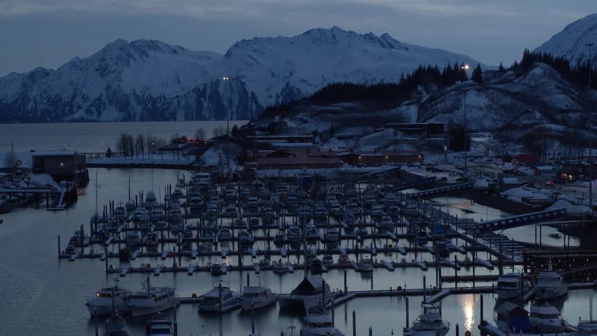 Slowly zooming out to reveal a quiet, snowy boat harbor in a remote mountain town at dusk