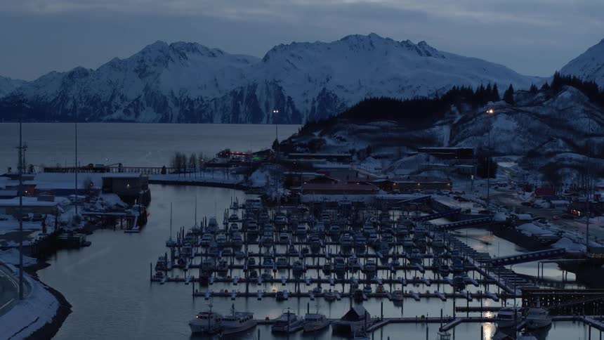 A slow zoom out reveals a quiet, snow-covered harbor town nestled among majestic mountains at twilight