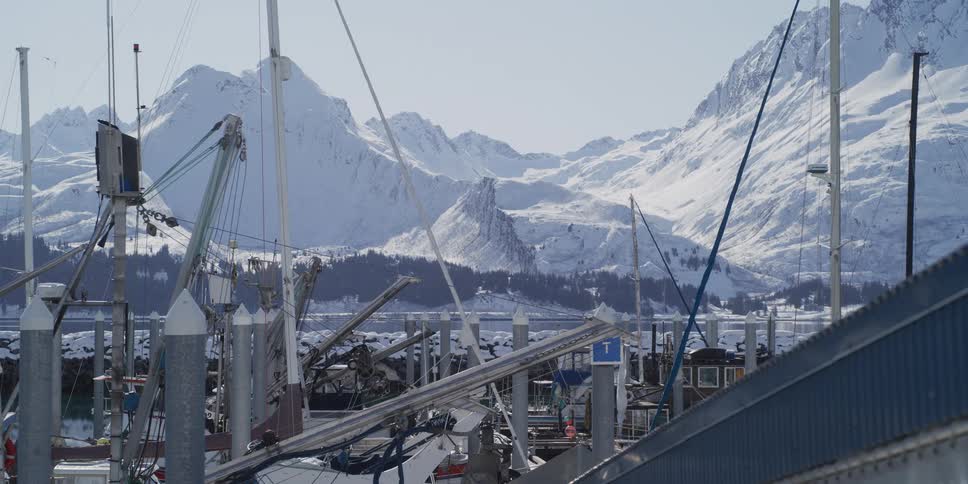 A fishing boat harbor sits peacefully on a sunny winter day with a majestic snow-covered mountain range in the background