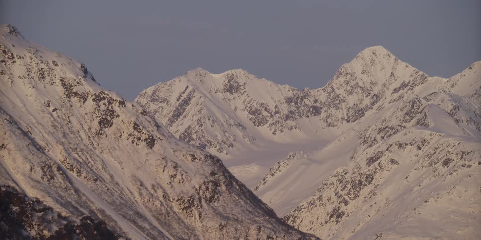 A stunning static shot captures majestic snow-covered mountain peaks basking in the warm glow of sunrise or sunset
