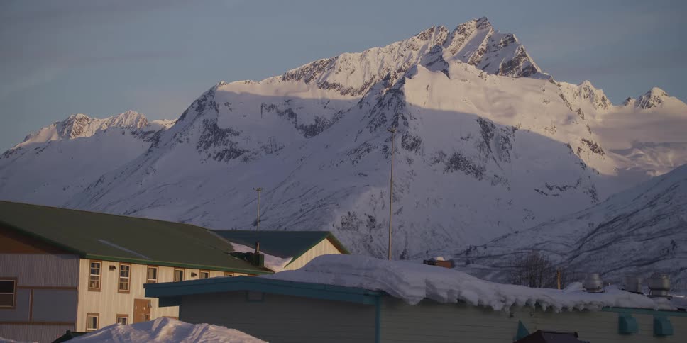 Majestic snowy mountains stand tall over a snow-covered town in the early morning light