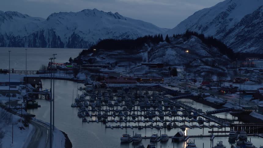 A slow zoom-out timelapse reveals the tranquil beauty of a snowy harbor town in Alaska at twilight