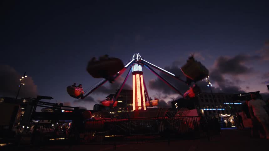 A brightly lit carnival ride spins guests high into the air against a twilight sky at an urban fair