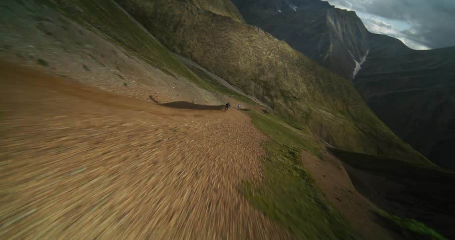 Dynamic drone footage follows a group of extreme mountain bikers as they race down a steep, dusty trail in a majestic mountain range