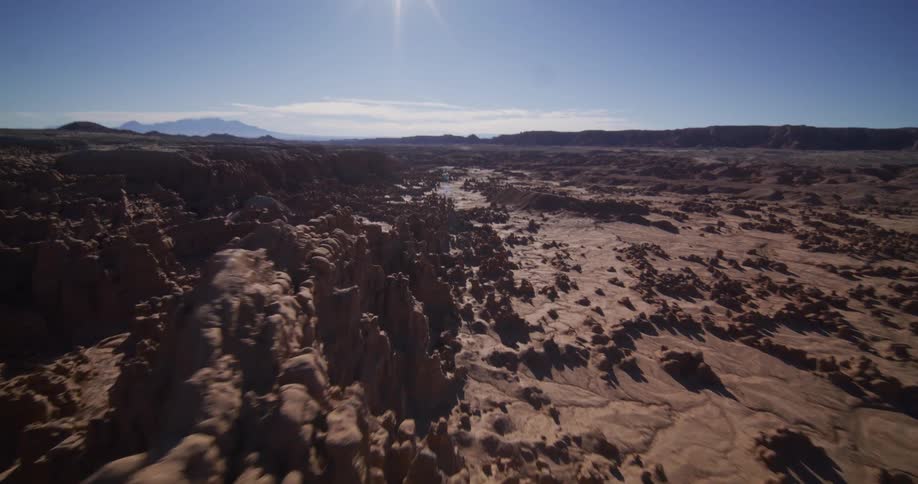 A slow aerial pullback reveals the vast, sun-drenched landscape of Goblin Valley State Park in Utah, showcasing its unique hoodoo rock formations