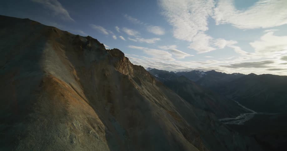 A stunning aerial shot pulls back over a vast and rugged mountain range revealing an expansive valley at sunrise