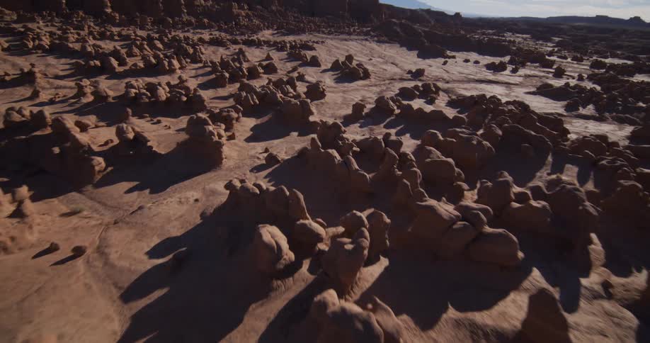 A stunning aerial shot starts from a top-down view and then tilts up while descending over the unique hoodoo rock formations in a vast desert valley