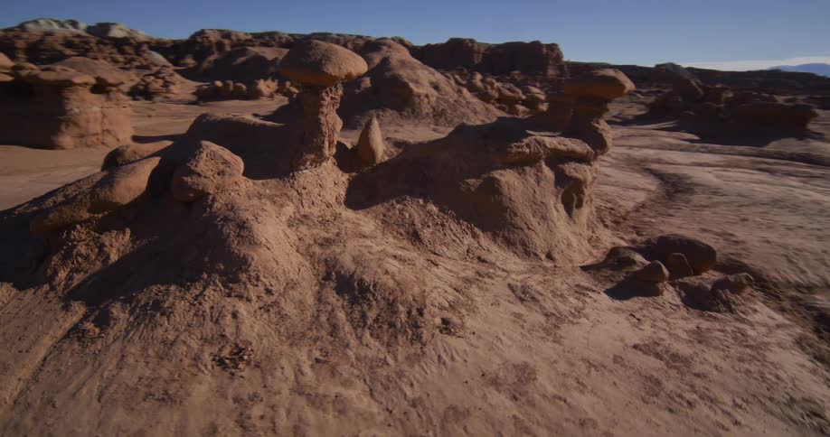 Slow, cinematic drone footage pans across the unique geological hoodoo formations in a desert valley under a clear blue sky