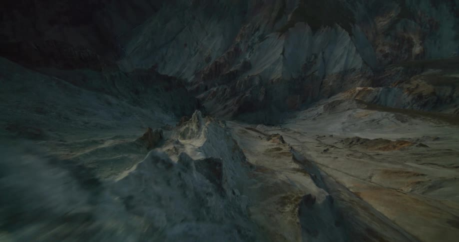 An epic aerial flight moves over a desolate and rocky mountain range in the dim light of dusk