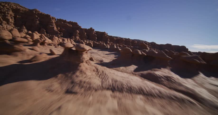 An immersive aerial fly-through of the surreal red rock formations of Goblin Valley State Park on a clear sunny day