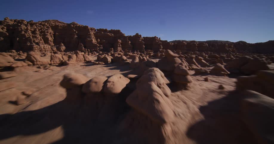 A stunning aerial fly-through reveals the unique and otherworldly landscape of Goblin Valley's hoodoo rock formations under a clear blue sky
