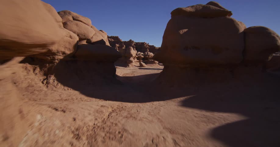A smooth tracking shot glides through the fantastical, otherworldly hoodoo rock formations of Goblin Valley State Park in Utah under a clear blue sky