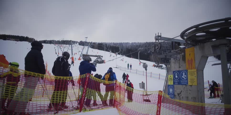 A group of skiers waits in line for a T-bar ski lift at a bustling resort on a cloudy winter day