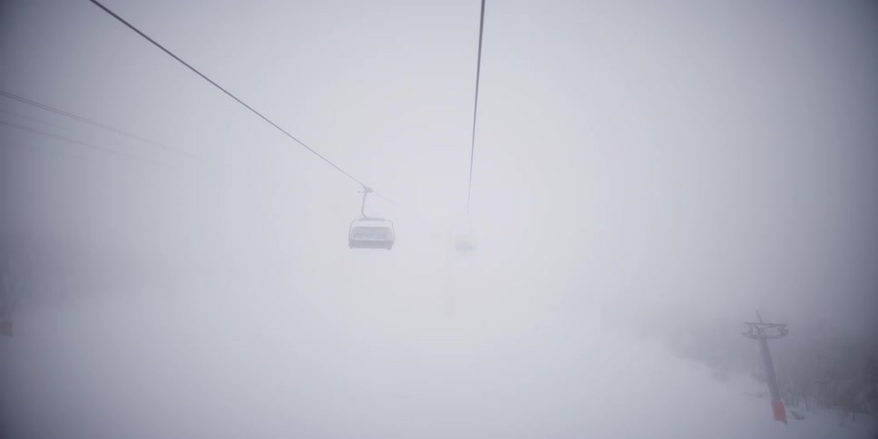Eerie POV from a ski lift ascending through a thick, snowy fog, with empty chairs appearing and disappearing in the whiteout