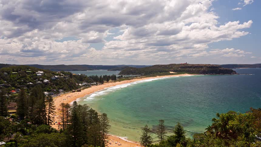 A scenic high-angle view of a popular crescent-shaped beach with turquoise water as people enjoy a sunny day under a partly cloudy sky