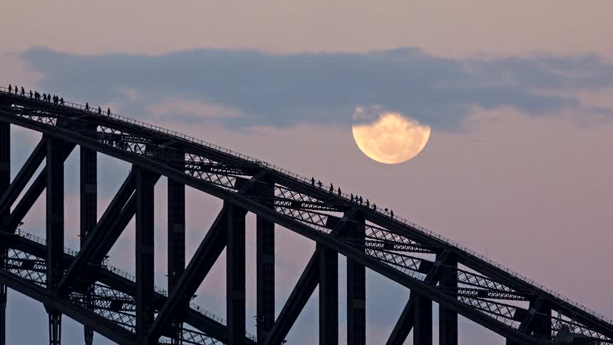 A stunning timelapse of the full moon rising behind the iconic Sydney Harbour Bridge as people walk across the arch at dusk