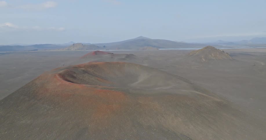 An aerial view rises to reveal a vast, desolate volcanic landscape with multiple red and black craters