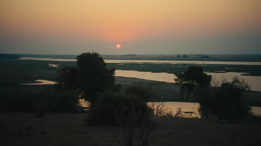 A beautiful sunset casts a warm golden glow over a tranquil river delta in the vast African savanna