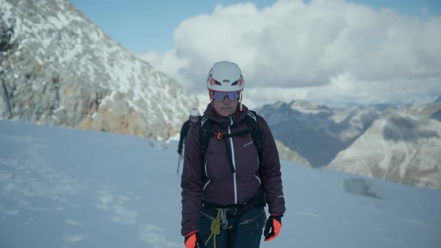 A female mountaineer walks towards the camera in slow motion while trekking through the snow in a vast mountain range