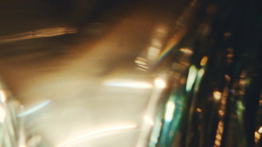 Shimmering golden and green light flares refract and distort, creating a mesmerizing abstract visual with bokeh effects