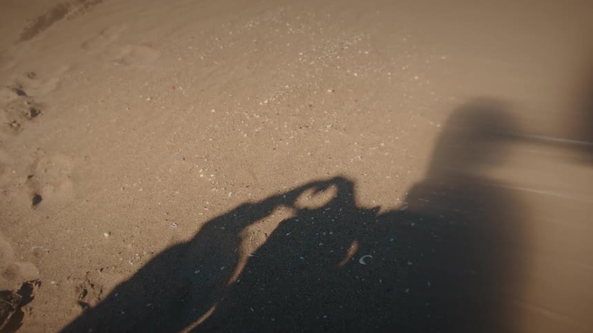 Shadows of a romantic couple making a heart shape with their hands on the golden sand