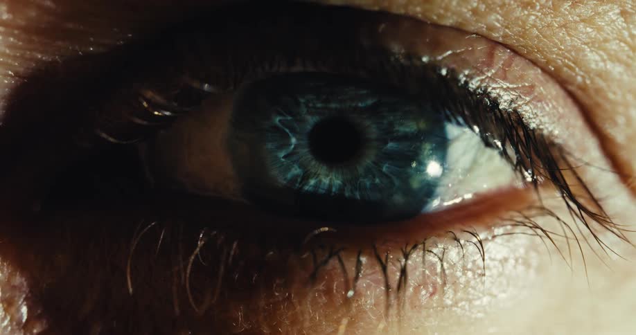 A dramatic, extreme macro shot of a wet, blue human eye slowly opening and staring