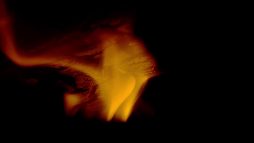 An intense close-up shot shows a piece of paper smoldering and burning in slow motion against a dark background