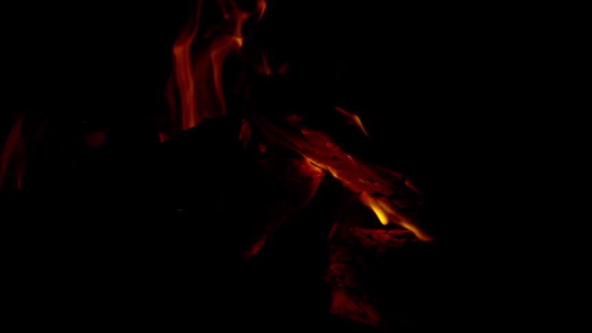 Warm flames flicker in slow motion over burning logs against a dark background