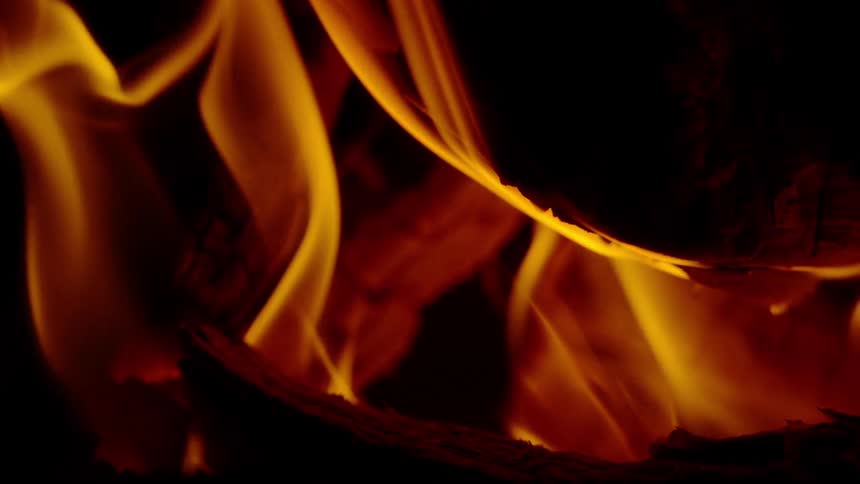Hypnotic slow-motion flames flicker and dance over burning wood in the dark