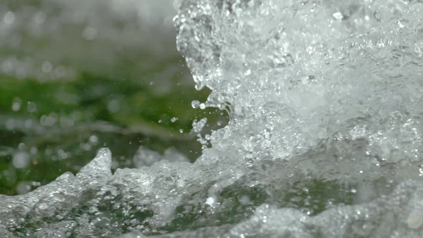 An extreme close-up of churning river water is captured in stunning super slow motion, highlighting the bubbles and spray