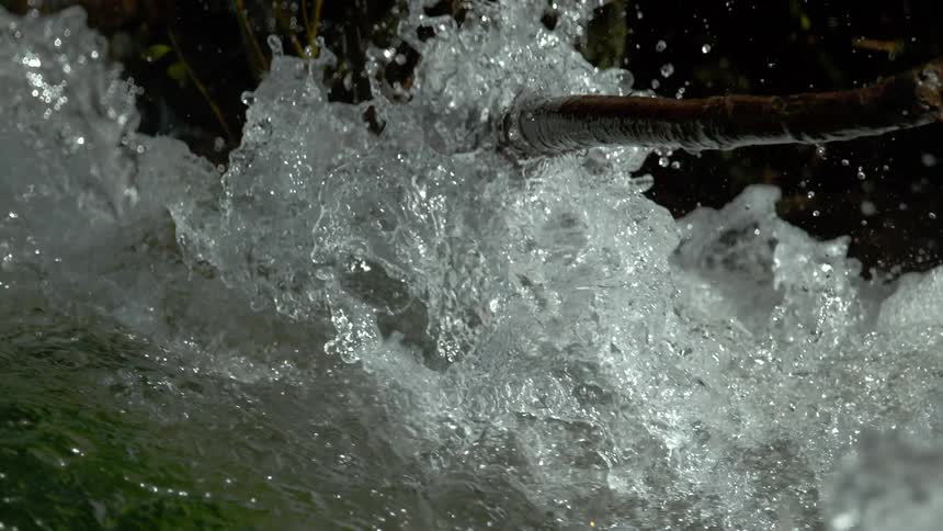 Crystal clear water from a mountain stream crashes against a fallen branch in super slow motion