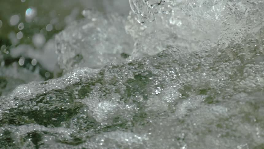 A super slow-motion close-up of water bubbling and churning in a fast-flowing river