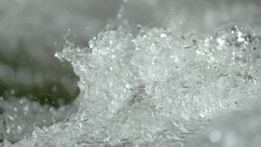 A mesmerizing slow-motion macro shot captures the raw power of churning river water as it splashes and sparkles in the light
