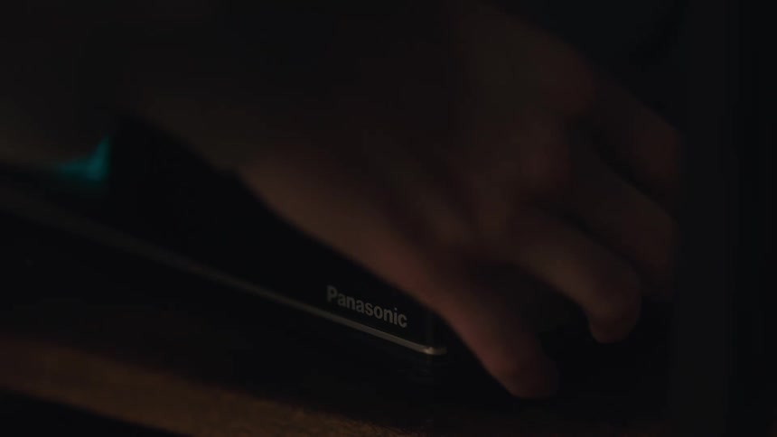 A hand turns the dial on a vintage Panasonic alarm clock radio in a dark room