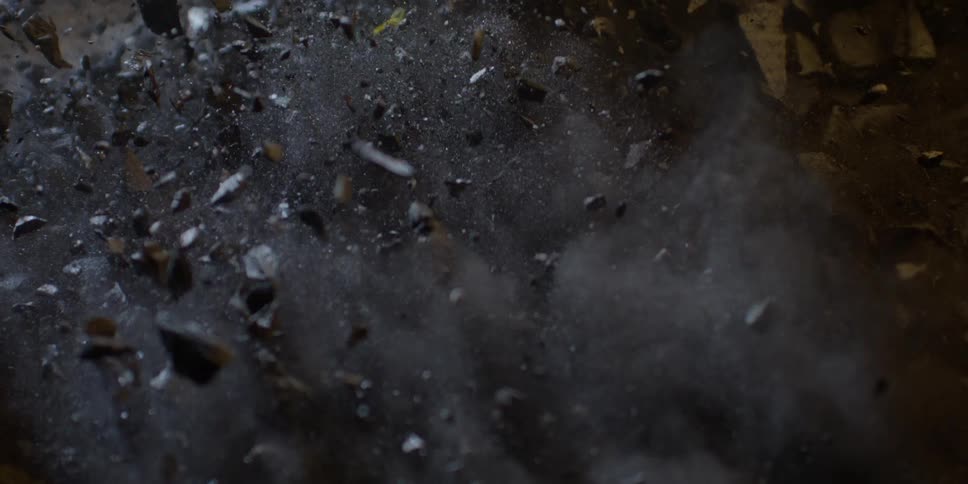 A dramatic super slow motion close-up of dark rocks and dust exploding