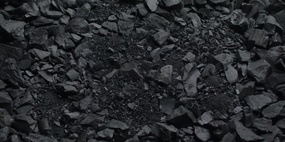 Charcoal dust falls onto a pile of charcoal chunks in dramatic slow motion