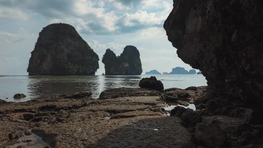 Majestic limestone islands stand in the calm ocean, revealed by a slow dolly shot from a rocky tropical shore