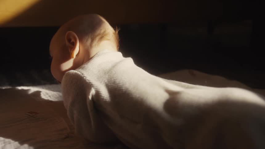 A newborn baby lifts its head for the first time during tummy time in a warm sunbeam
