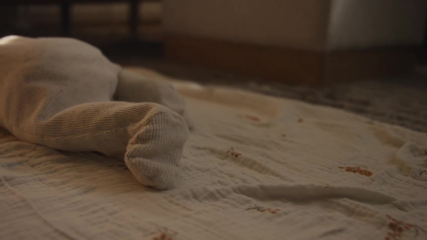 A close-up of a newborn baby's tiny feet in white footie pajamas wiggling on a soft blanket