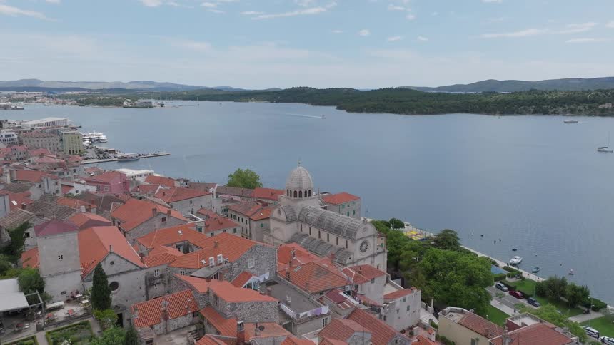 Slow aerial push-in shot reveals the historic coastal city of Šibenik, Croatia, highlighting the iconic Cathedral of St. James by the Adriatic Sea