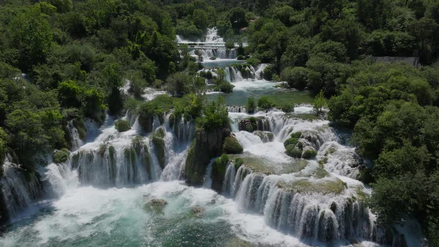 An immersive aerial view flying towards the stunning multi-tiered waterfalls of a lush national park