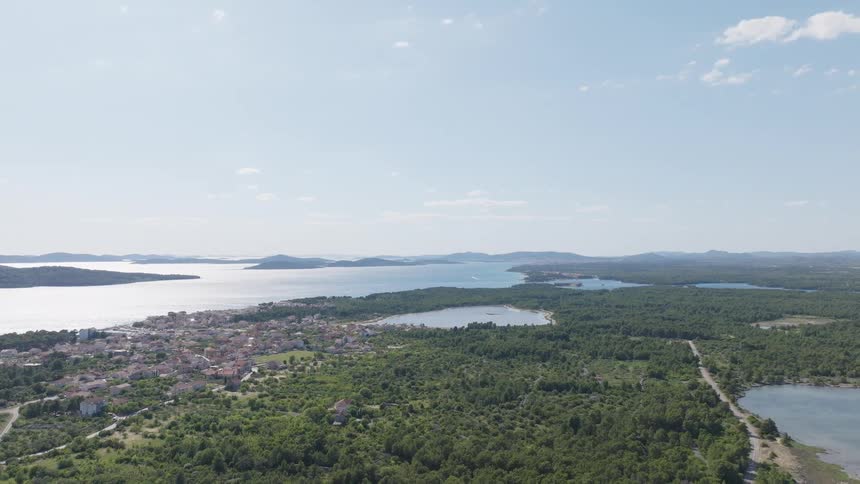 Stunning aerial wide shot of a European coastal town surrounded by lush green forests and the serene blue sea